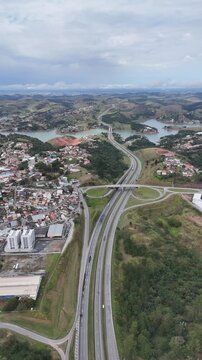 Panorama a&eacute;reo de rodovia pr&oacute;xima Igarat&aacute;, SP, revelando curvas e pistas, &aacute;reas verdes e colinas sob um c&eacute;u parcialmente nublado, em uma paisagem rural do interior de S&atilde;o Paulo.