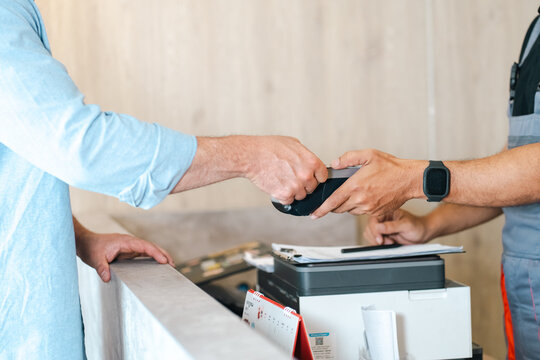 Electric vehicle battery car service Man making contactless payment at service counter with card terminal during customer transaction