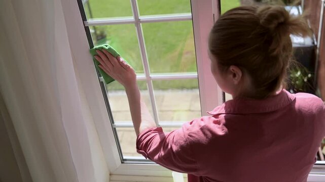 Woman washes window with green cloth and spray detergent. Spring cleaning housework concept