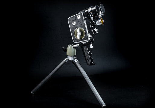 Vintage 16mm movie camera from the 1960s on a tabletop tripod. Antique analog film video camera, retro cinematography equipment backdrop in low key lighting.