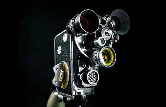 Vintage 16mm movie camera from the 1960s on a tabletop tripod. Antique analog film video camera, retro cinematography equipment backdrop in low key lighting.