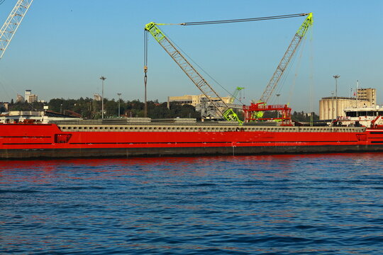 View of a large red cargo ship equipped with cranes navigating the Bosphorus strait in Istanbul, Istanbul, Turkiye.