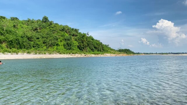 Tranquil river water along forested island beneath bright blue sky - panning shot.