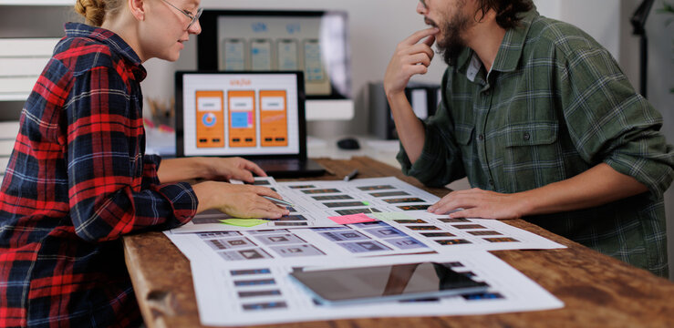 Designers collaborating on web development project. Reviewing uiux wireframes and application interfaces on printed mockups and laptop screen