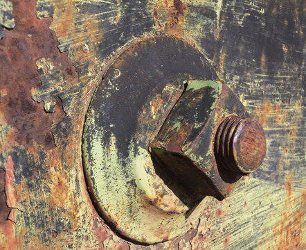View of a large, rusted metal bolt and nut attached to a weathered, peeling painted metal surface in the historic ghost town of Rhyolite, Nevada, United States.