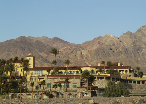 View of Furnace Creek Inn with its historic stone architecture and surrounding palm trees set against the rugged Amargosa Mountains in Death Valley, California, United States.