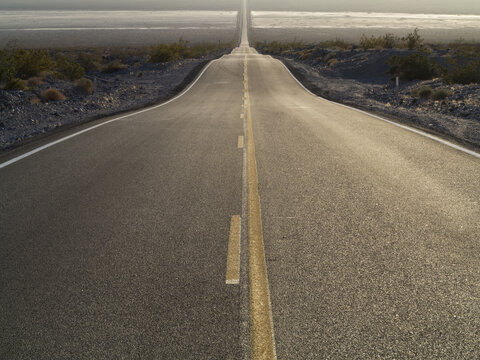 View of a long, straight asphalt road stretching into the horizon through the desert landscape of Death Valley National Park in Death Valley, California, United States.