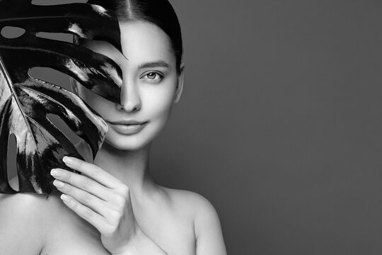 Close up woman face with green exotic leaf. Skin care beauty treatments concept. Model with clean, health skin of face. Monstera Leaves