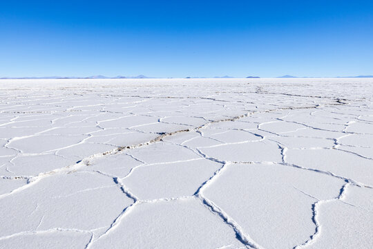 View of the Uyuni Salt Flat with its iconic white hexagonal salt crust patterns under a clear blue sky in Bolivia.