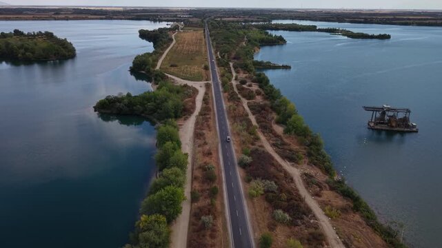 An aerial perspective shows a lonely road dissecting tranquil blue lakes with an industrial barge present offshore.