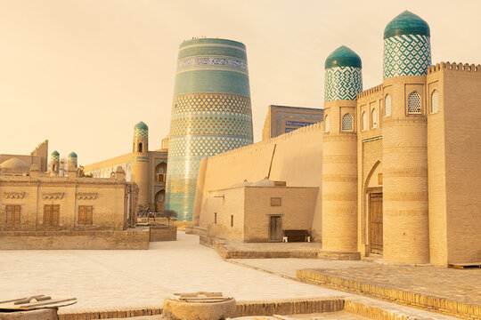 Kalta Minor minaret and historic brick buildings in Ichan Kala, Khiva, bathed in warm golden light. This iconic Uzbekistan landmark image is ideal for travel publications, tourism brochures.