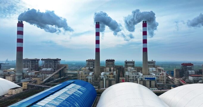 An aerial view of an industrial thermal power plant with three tall smokestacks emitting thick white steam under bright natural light.