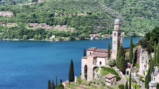 Morcote Switzerland lakeside church and bell tower framed by cypress trees on Lake Lugano shoreline, Ticino alps in background.