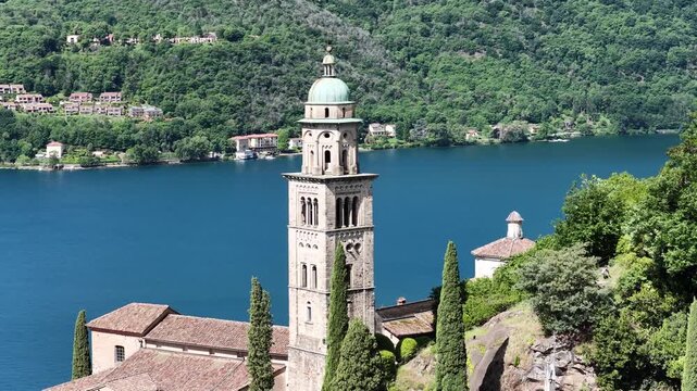 Morcote Switzerland aerial of lakeside bell tower and church rooftops, deep blue Lake Lugano stretching into forested hills.