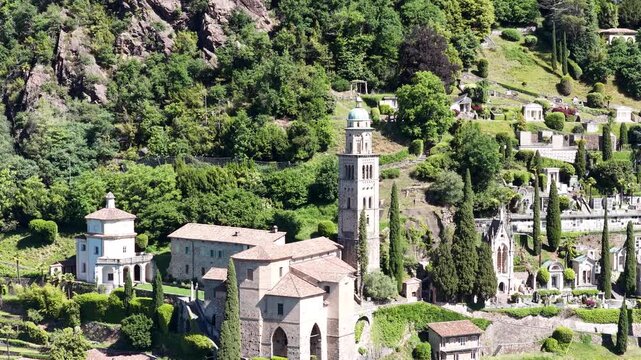 Morcote Switzerland aerial view of hillside church, bell tower and terraced cemetery surrounded by cypress trees and forest.