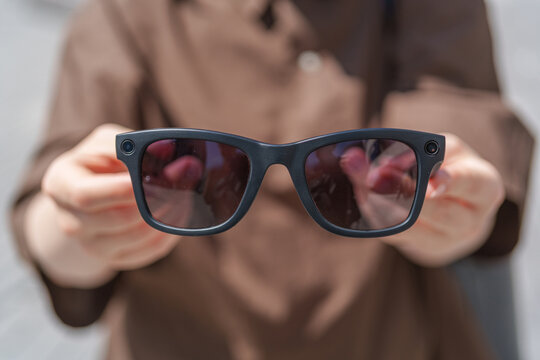Person holding smart glasses with integrated camera outside in bright sunshine