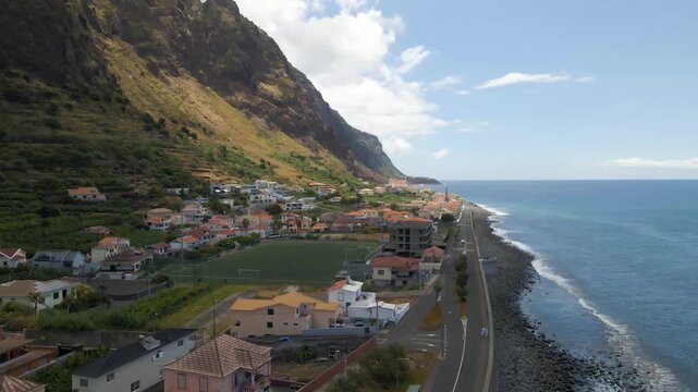 aerial shot of Paul do Mar village stretched along a thin strip of land between mountains and sea. Composition highlights the unique geography of Madeira Island and resilience of coastal communities.
