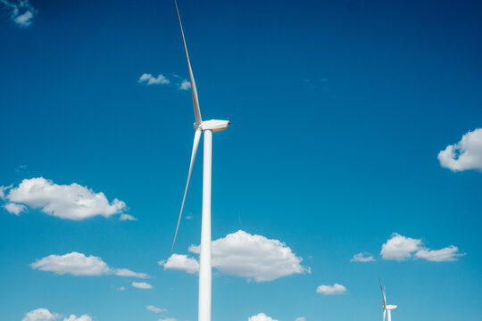 View of Wind farm Alibunar with white wind turbines standing against a clear blue sky with scattered white clouds in Alibunar, Vojvodina, Serbia.