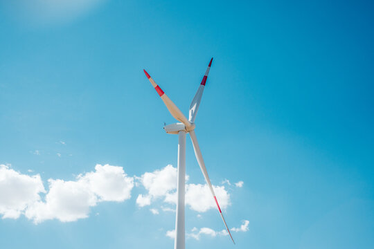 View of Wind farm Alibunar, a large wind turbine with red-tipped blades standing against a clear blue sky with light clouds in Alibunar, Vojvodina, Serbia.