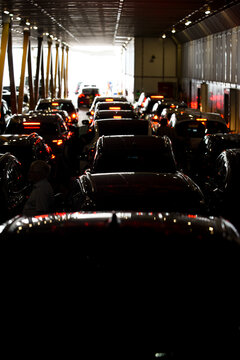 View of cars parked inside a ferry deck with a bright exit in the background and a man standing near a vehicle in Denmark.
