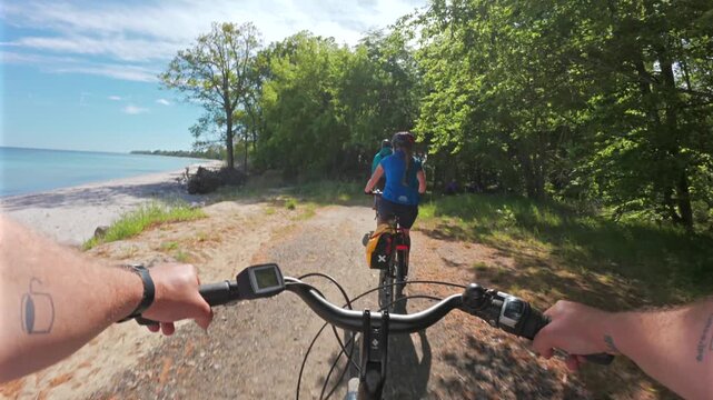 First-person chest-mounted view riding an electric bike along a wooded coastal section of the EuroVelo 10 route with the Baltic Sea visible on the left in Denmark on a sunny day