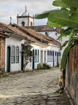 View of the historic colonial architecture with white walls and blue trim along a cobblestone street in the old town of Paraty, Rio de Janeiro, Brazil.