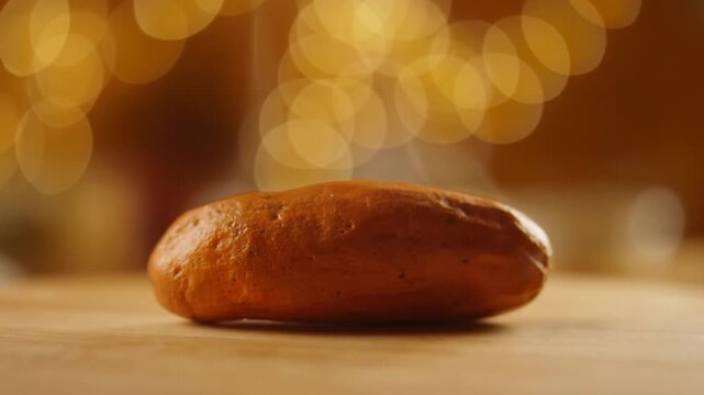 Golden-brown bread roll resting on a wooden tabletop in warm indoor light. Bakery advertising, bread packaging promotion, and food marketing.