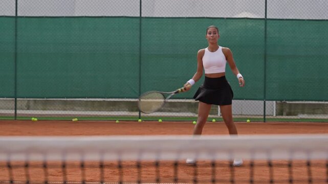 Young Biracial woman playing tennis on clay court, returning balls with forehand and backhand strokes. Footage suitable for sports marketing, athletic training campaigns and fitness commercials