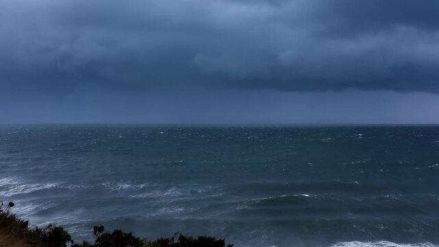 Stormy ocean coastline with rolling waves, heavy rain and lightning beneath dark clouds. Weather news, storm documentary, and climate education.