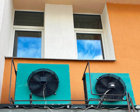  industrial air conditioner compressor units mounted on a colorful orange building wall below glass windows, ideal for HVAC services promotion, urban infrastructure articles and climate control techno