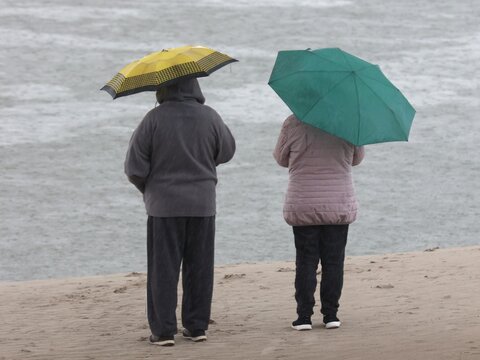 Vue de derri&egrave;re de deux personnes debout face &agrave; la mer portant leur parapluie jaune et vert ouverts. Temps pluvieux devant l'oc&eacute;an. 