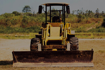 Front view of yellow bulldozer with large blade parked on dirt field with trees in background © Muhamad