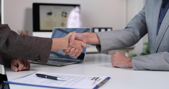Business partners shaking hands at an office desk, finalizing a successful agreement, partnership, or deal after a productive meeting and interview in a modern corporate setting