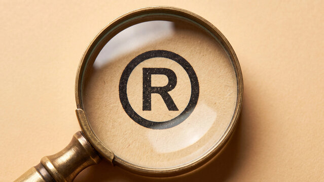 Registered trademark symbol viewed through a classic vintage magnifying glass with brass frame on a textured light brown paper surface