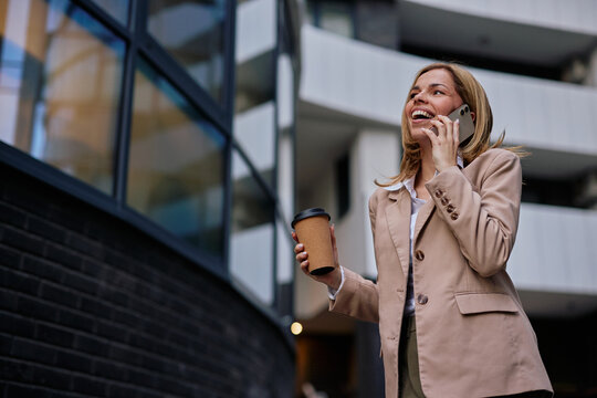 Businesswoman talking on phone holding coffee walking city