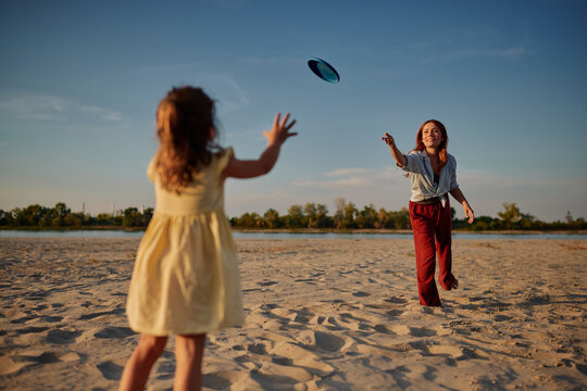 Mother and daughter playing frisbee at sunset on beach