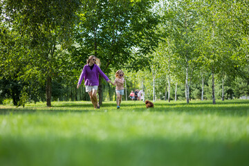 Fototapeta premium Mother and little girl holding hands and running across a green park lawn