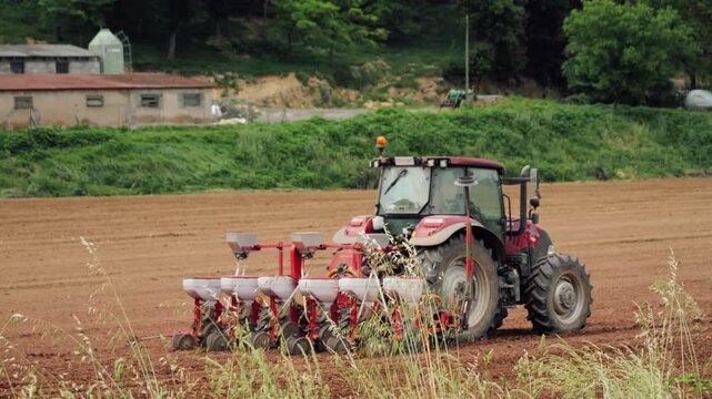 Tractor sowing a cultivated agricultural field in the countryside. Modern farming machinery working on farmland during planting season. High quality 4k footage