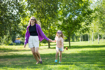 Fototapeta premium Mother and young daughter holding hands while walking on park grass outdoors
