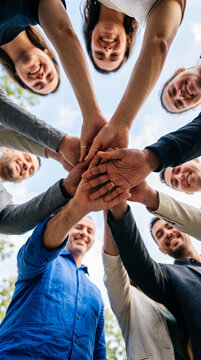 Diverse group of smiling people stacking hands, symbolizing unity, teamwork, and collaboration, perfect for business or lifestyle concepts.