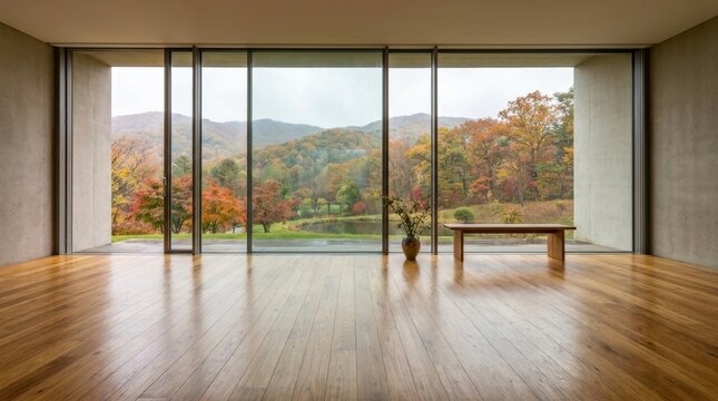 Modern minimalist interior with large windows overlooking autumn forest landscape.