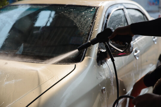 Car cleaning with pressure washer, hand washing vehicle with high pressure water spray for car wash and auto care, removing dirt from automotive surface during vehicle cleaning.