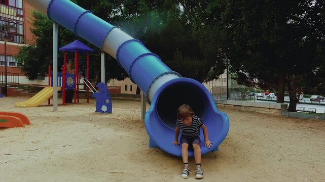 Happy boy sliding down a playground tube slide in slow motion