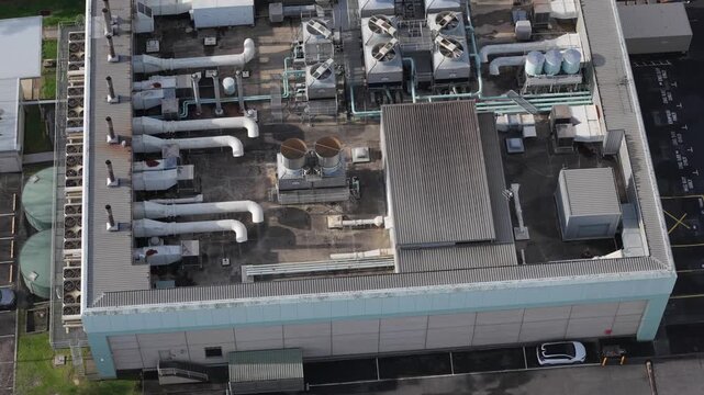Aerial drone footage of industrial data centre rooftop showing HVAC cooling units, metal ductwork, corrugated metal structures and air handling equipment in bright daylight. Gray and blue toned indust