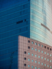 A modern building with blue glass facades and a curved corner stands beside a brick structure, creating an intriguing geometric architectural contrast. © Faies