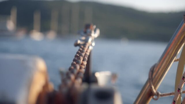 Sailboat anchored in a bay during sunset with focus on the chain and rigging