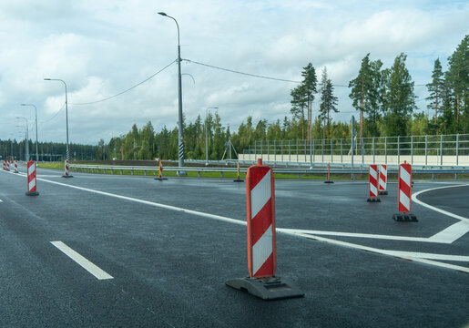 Red and white plastic barriers marking closed lane on empty asphalt highway road. Road construction and traffic safety warning signs.