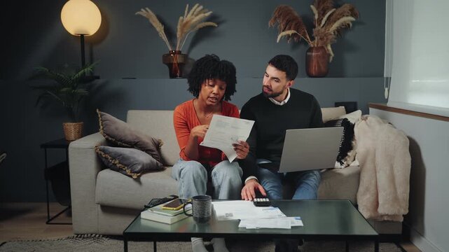 Concerned young couple sitting on a couch at home calculating expenses and managing family finances and domestic economy