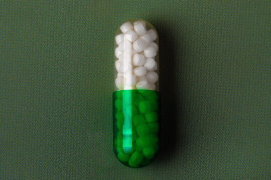 Close-up of a green and white capsule pill on a textured green background, symbolizing medicine, health, or pharmaceuticals.