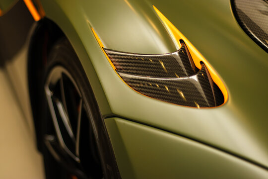 Krakow, Polska - September 06, 2026: Close-up view of a luxury sports car's carbon fiber air intake and sleek green bodywork with orange accents in a modern showroom